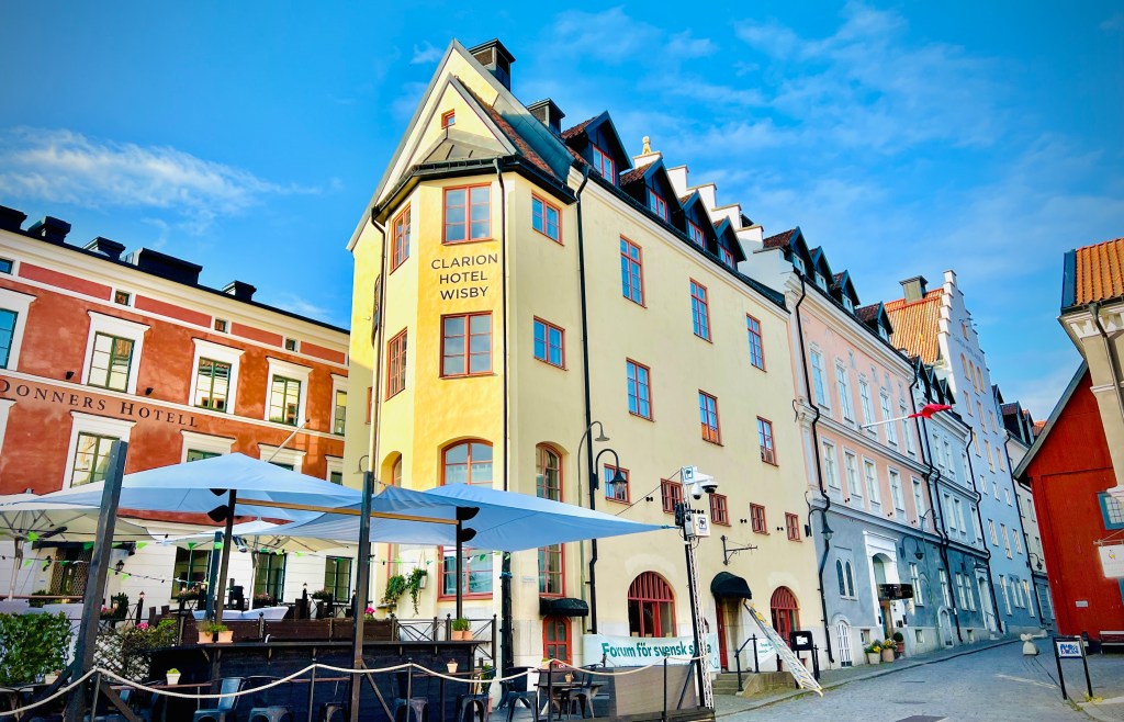 A charming street view in Visby, Gotland, featuring the Clarion Hotel with colorful historic buildings and outdoor seating.